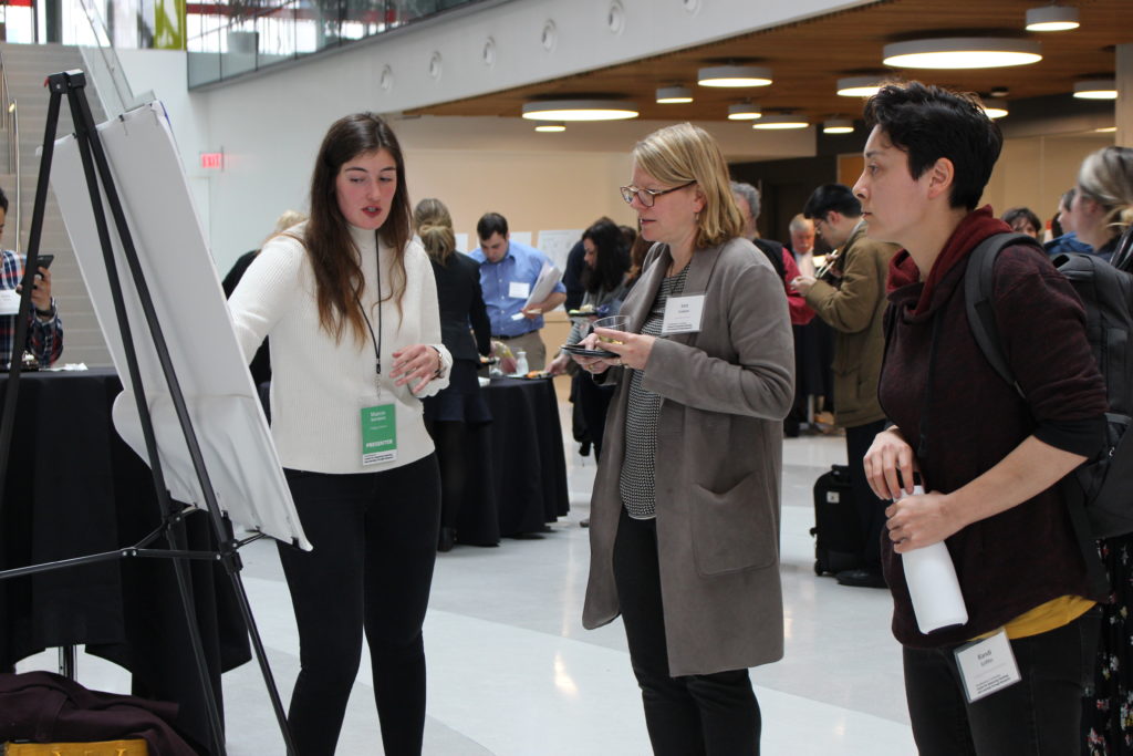 A white, female graduate student presenting their poster to two female educators at CATLR's CAEBL conference in 2019.