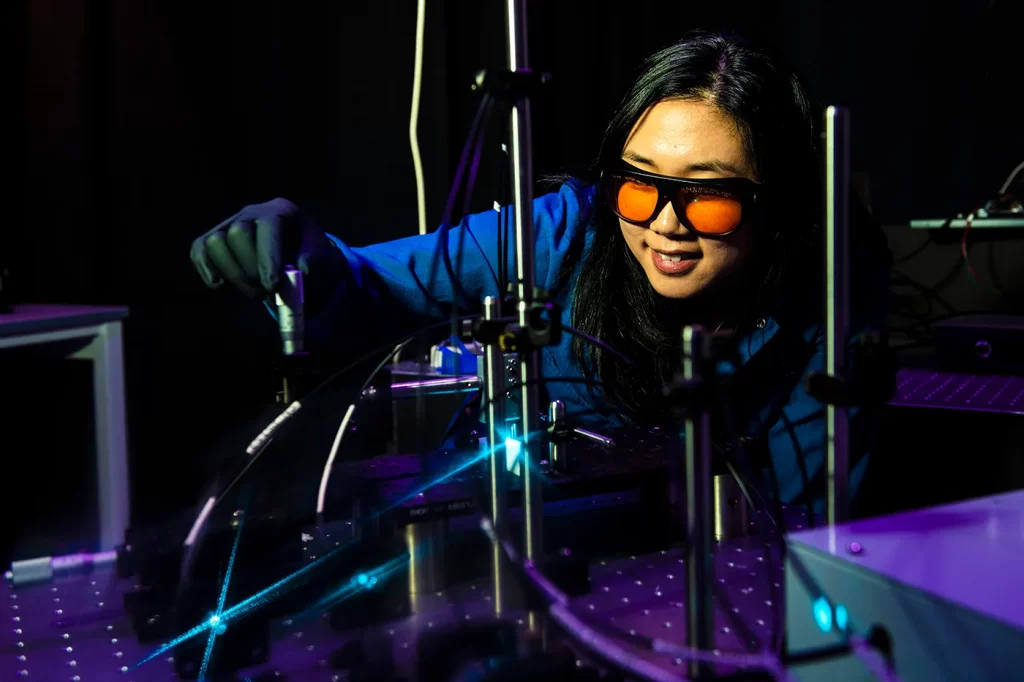An asian female student wearing lab goggles and gloves while working with equipment in a dark room.